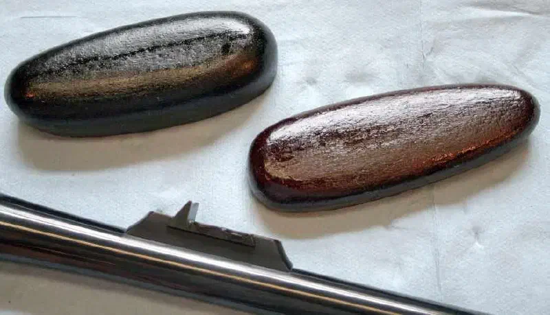 Pair of hand-formed leather wrapped recoil pads by Todd Ramirez, one finished black and one in brown, shown beside a polished rifle barrel
